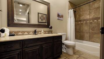 A bathroom with a dark wood vanity, a white toilet, and a shower with a beige tiled wall.