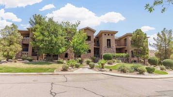 A multi-story residential building with a landscaped front yard, stone and stucco exterior, and a driveway leading to the entrance.