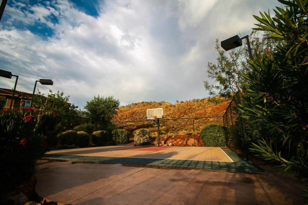Una cancha de baloncesto al aire libre con un aro, rodeada de vegetación y un paisaje montañoso al fondo.