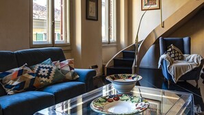 A modern living room with a glass coffee table, a blue sofa, and a staircase with a chair. - Borgo San Lorenzo 11 (Florence)