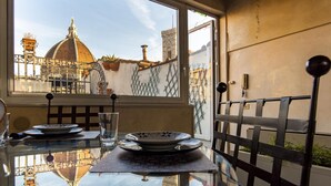 A table with plates and a glass, a window with a view of historical buildings, and a metal railing. - Borgo San Lorenzo 11 (Florence)