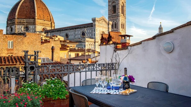 A rooftop terrace with a table set for a meal, overlooking historic buildings and a tower. - Borgo San Lorenzo 11 (Florence)