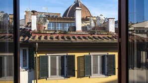 A yellow building with multiple windows and shutters, a dome-shaped structure in the background, and a clear blue sky. - Borgo San Lorenzo 11 (Florence)