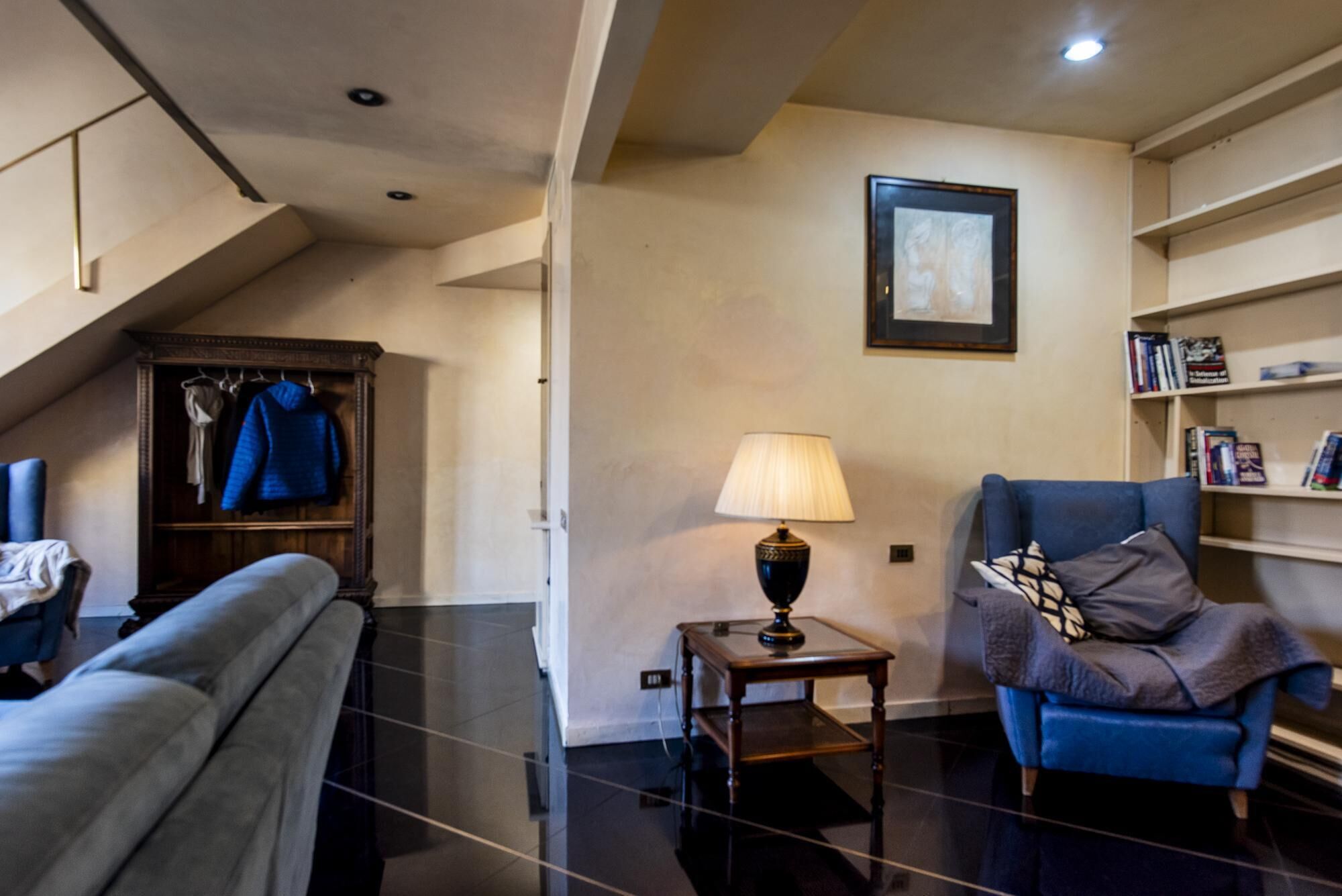 A modern living room with a sofa, a blue armchair, a wooden cabinet, and a table with a lamp.