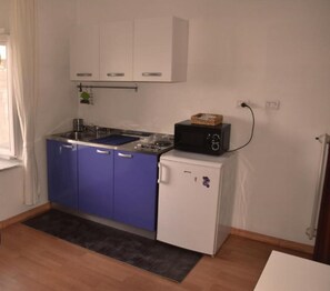 A compact kitchen with blue cabinets, a white refrigerator, and a microwave on top.