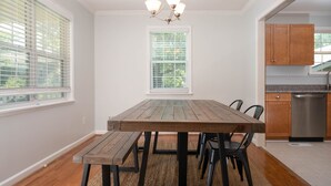 Un comedor con una mesa y bancos de madera, una araña y una cocina con armarios de madera y un refrigerador de acero inoxidable.