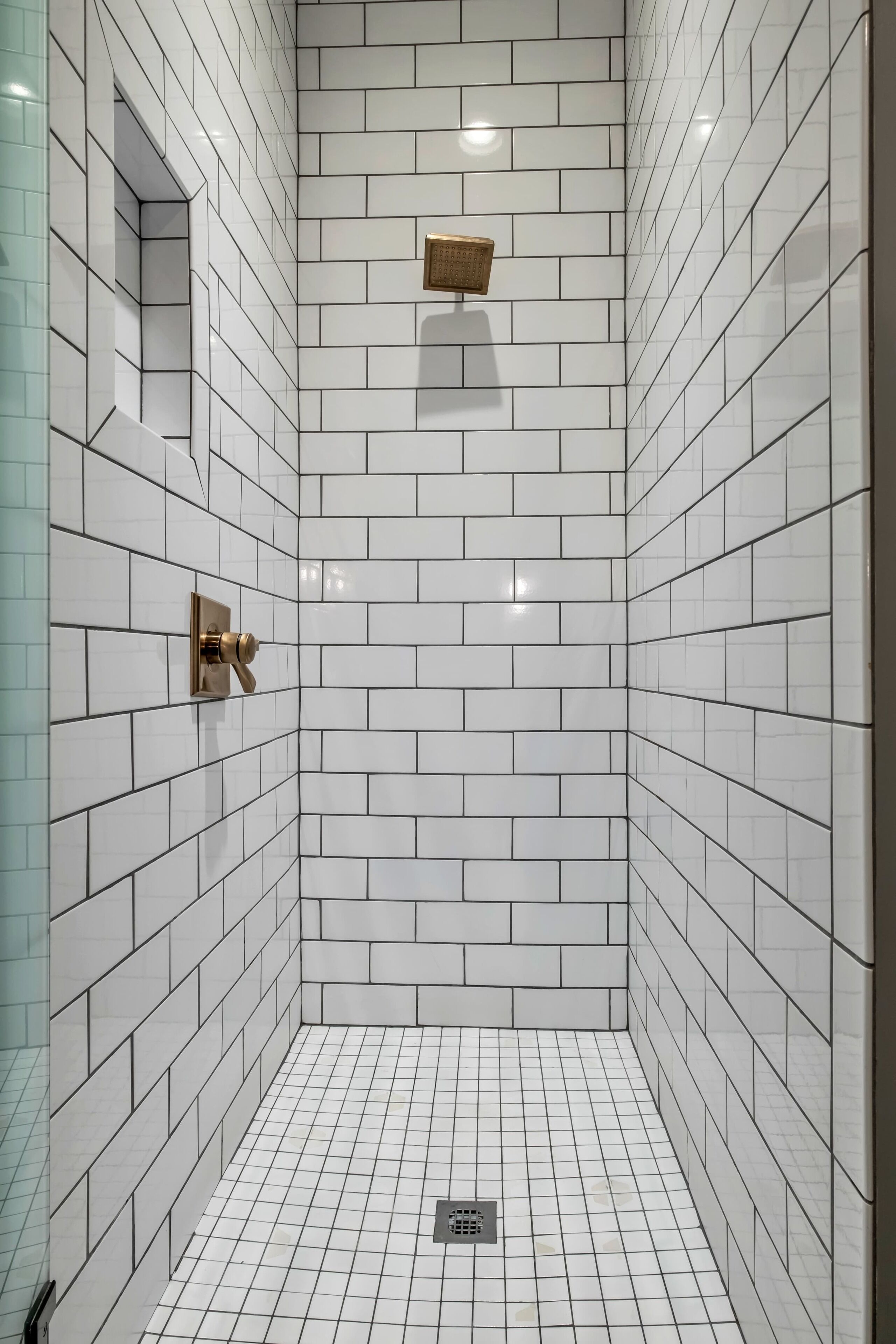 A shower with white tiles, a gold showerhead, and a small shelf.