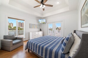 Un dormitorio con una cama grande, ventilador de techo, televisor y balcón con vista a edificios.