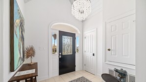 Un couloir avec une porte noire, des murs blancs, un lustre et une sculpture décorative.