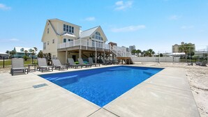 Une grande maison avec une piscine, une terrasse couverte et un espace clos aménagé avec des chaises longues.