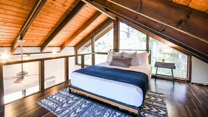 A bedroom with a large bed, wooden ceiling beams, and a view of the outdoors through large windows. - Oak Creeks Sedona Oasis with Hot Tub, and Hiking (Sedona)