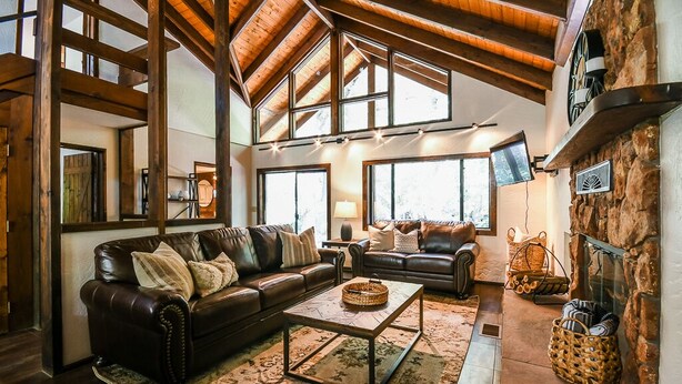 A cozy living room with a leather sofa, a coffee table, and a stone fireplace. - Oak Creeks Sedona Oasis with Hot Tub, and Hiking (Sedona)