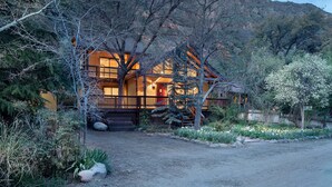 A rustic cabin with a wooden porch, surrounded by dense vegetation and a mountainous backdrop. - Oak Creeks Sedona Oasis with Hot Tub, and Hiking (Sedona)