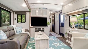Un intérieur de camping-car compact comprenant un canapé, un téléviseur, un coin cuisine et un espace repas.