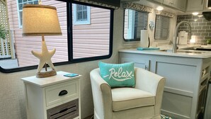 Un intérieur chaleureux avec un fauteuil blanc, une lampe en forme d’étoile de mer et un coussin orné du mot « Détente » sur un tapis turquoise.