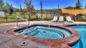Zona de piscina con jacuzzi, sillas de descanso y una zona sombreada.