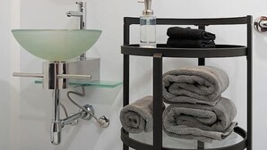 Ein Badezimmer mit einem Waschbecken aus Glas, einem Spiegel, einem Handtuchhalter mit Handtüchern und einem Toilettenpapierhalter.