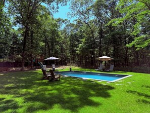 Un jardín trasero con piscina, rodeado de césped verde y árboles.