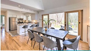 A spacious kitchen with a large island, a dining area with a wooden table and chairs, and a sliding glass door leading to a deck. - Upscale Hamptons Home: 1 Mi to Sammys Beach! (East Hampton)