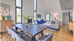 A spacious living area with a large wooden dining table, modern seating, and large windows providing natural light. - Upscale Hamptons Home: 1 Mi to Sammys Beach! (East Hampton)