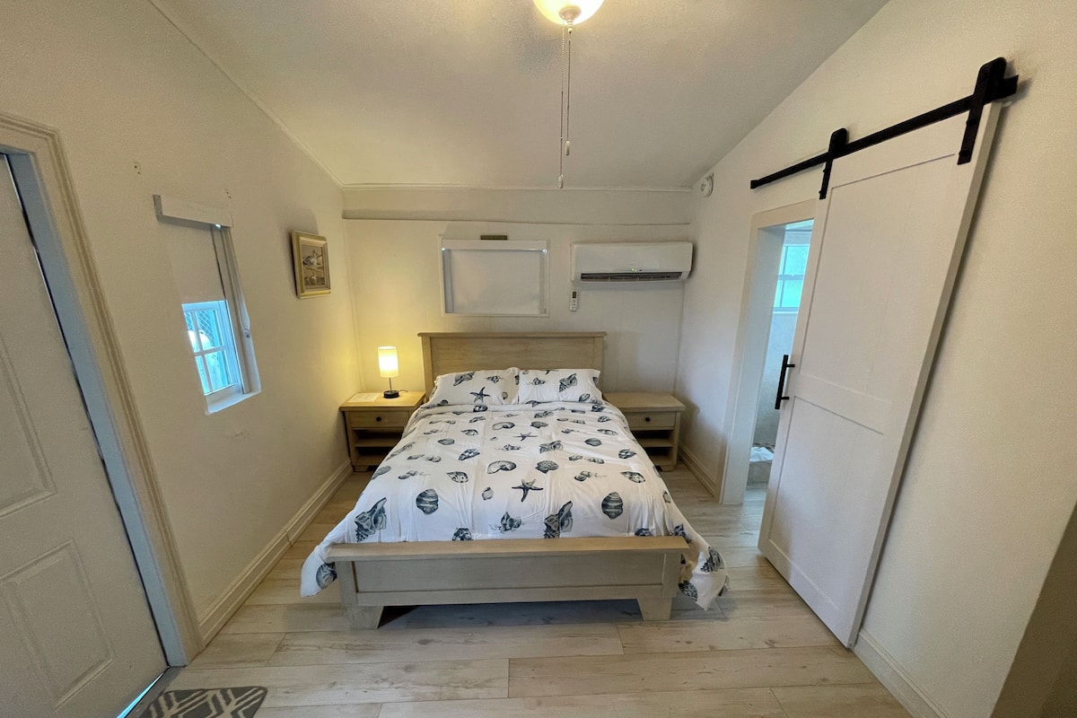 A bedroom with a bed, bedside tables, a nightstand, a window, and a door.