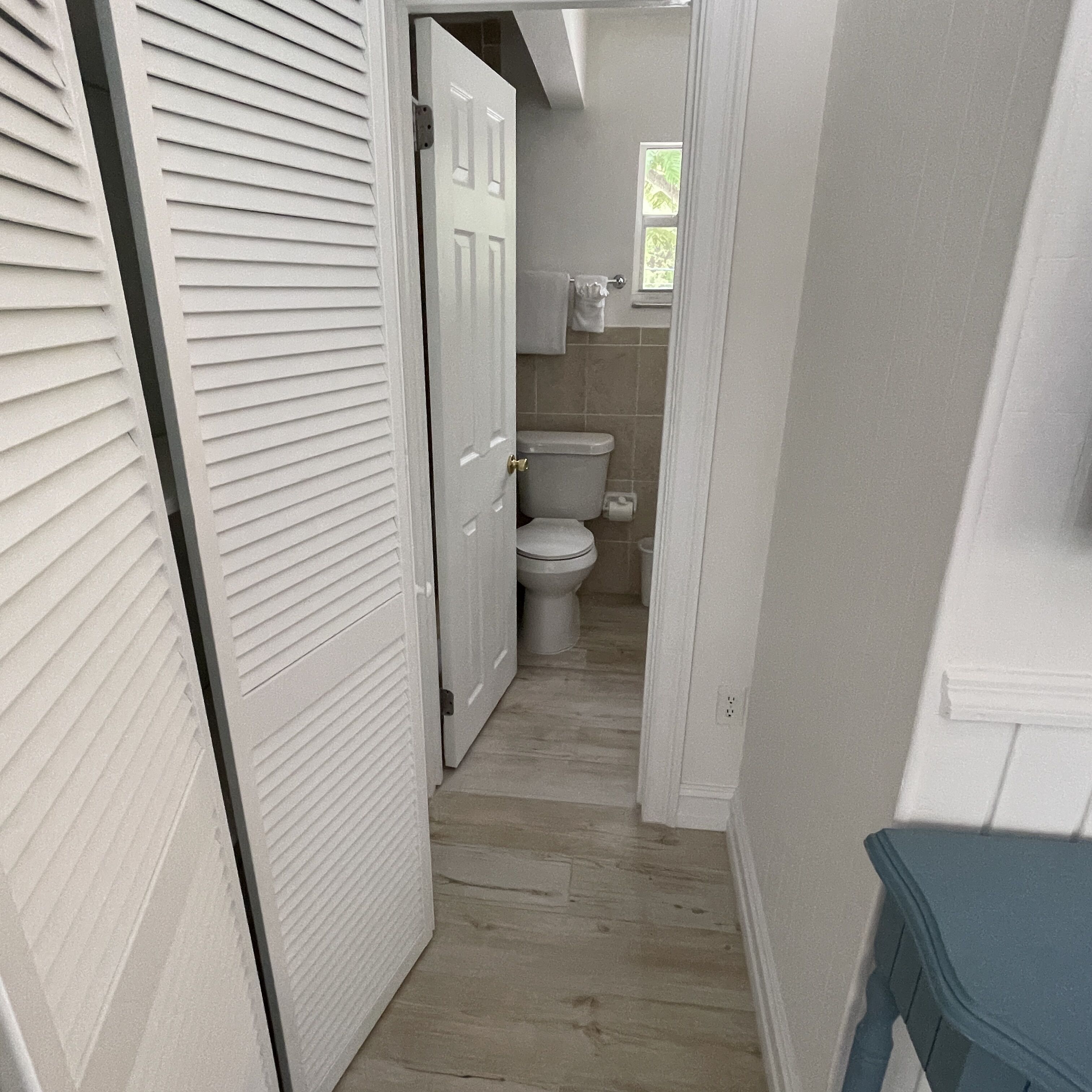 A narrow hallway leading to a bathroom with a toilet and a window.