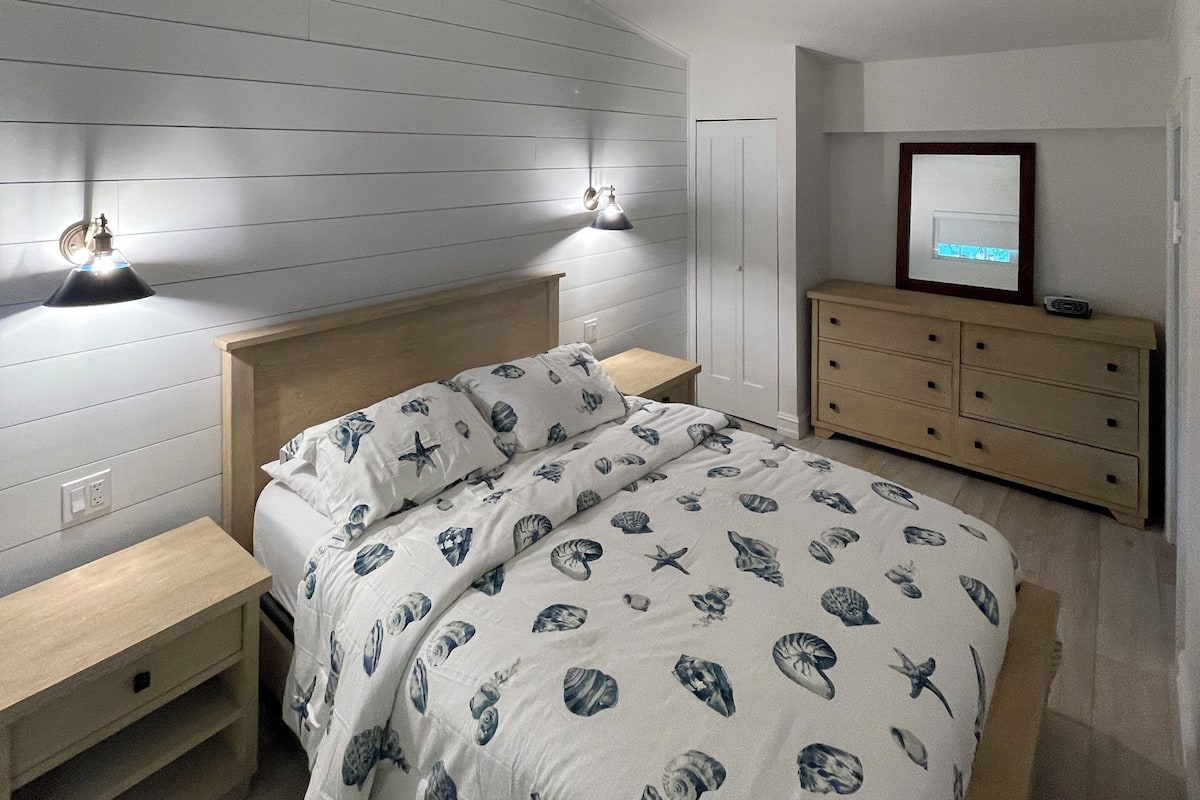 A bedroom with a bed, bedside tables, a dresser, a ceiling fan, and a wall-mounted lamp.