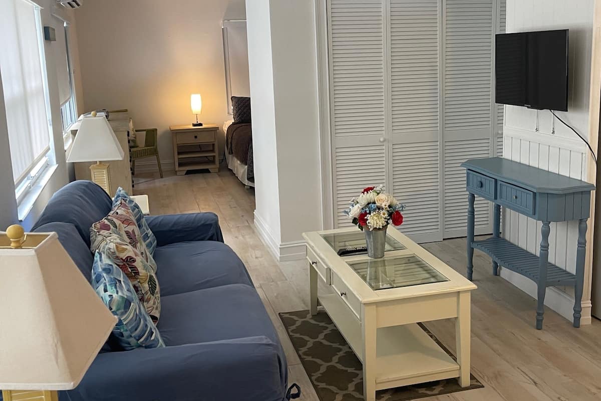 A living room with a sofa, a coffee table with a vase of flowers, a television mounted on the wall, and a sliding door closet.
