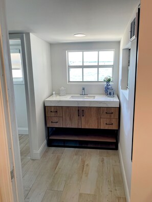 A modern kitchen with a white countertop, wooden cabinets, and a window above the sink.