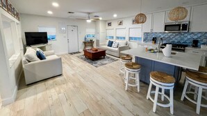 A modern kitchen with white cabinets, a microwave, and a stove. There is a dining area with a white table and stools. - Kings Kamp (Key Largo)