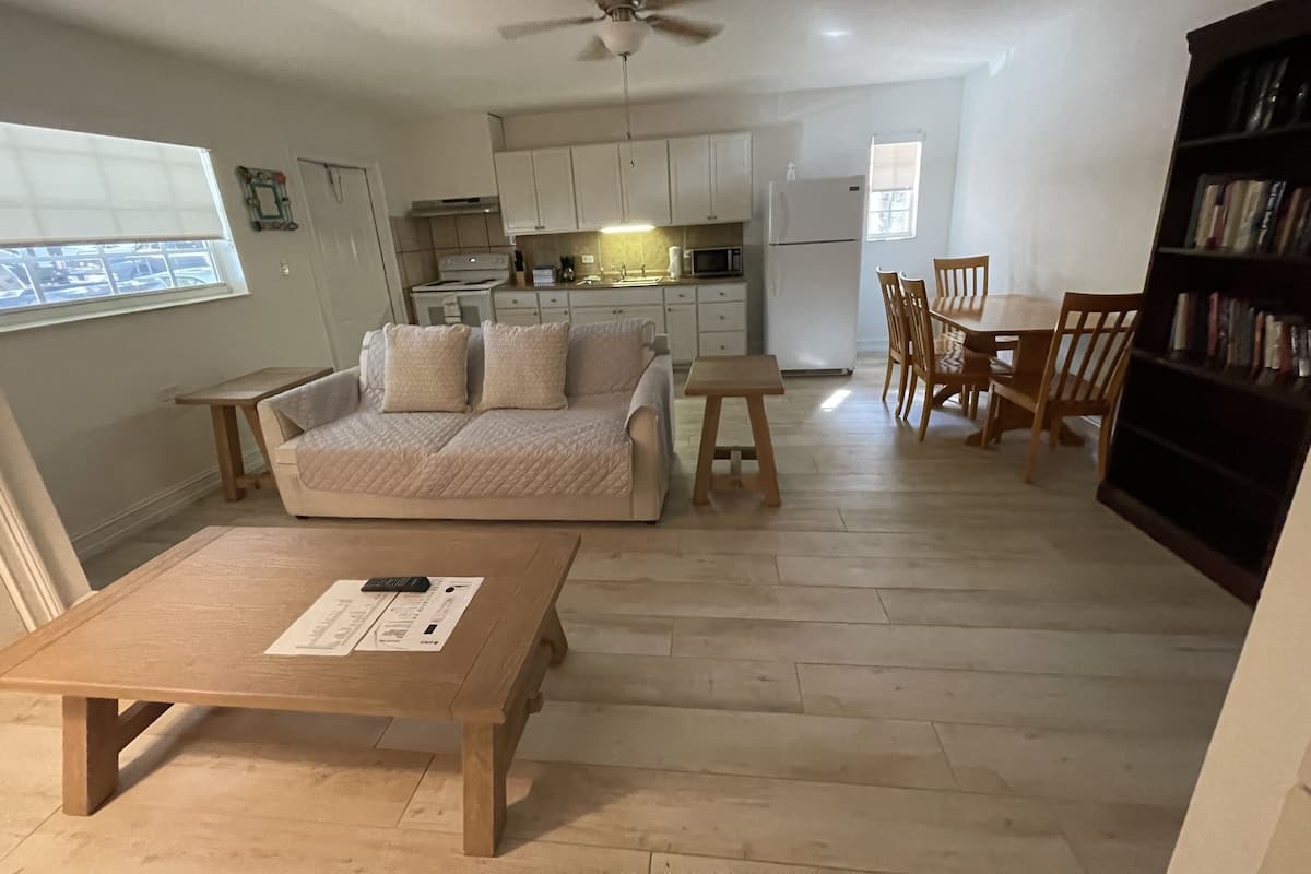 A compact living space with a sofa, a dining table, a bookshelf, and a kitchenette.