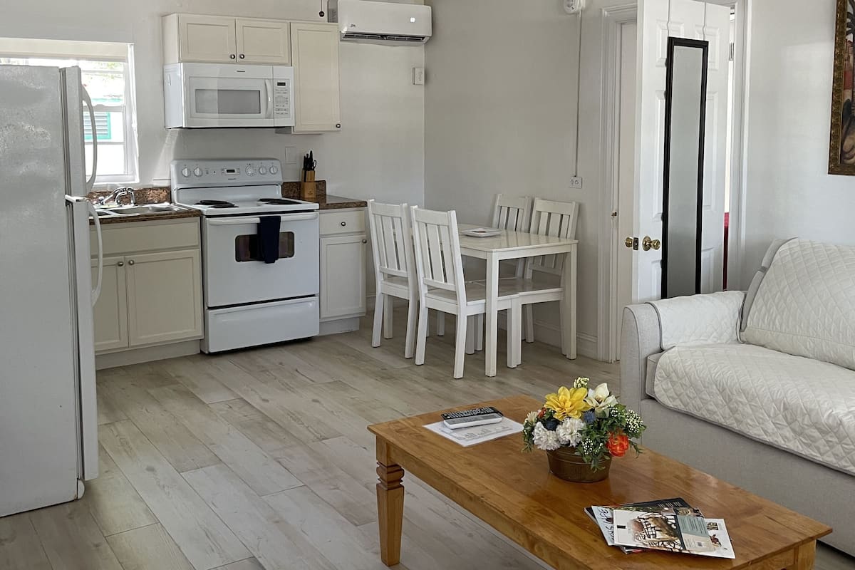 A compact kitchen with white cabinets, a microwave, stove, and a ceiling fan. There's a dining table with chairs and a sofa in the living area.