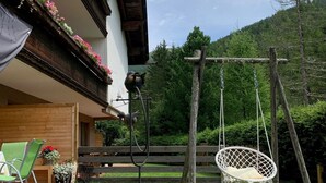 Ein rustikales Holzhaus mit einem Balkon, der mit Blumen geschmückt ist, einer Schaukel und einem Hängesessel in einem üppigen Garten.
