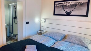 Ein Schlafzimmer mit Bett, Nachttisch, einem Gemälde und einer Duschkabine.