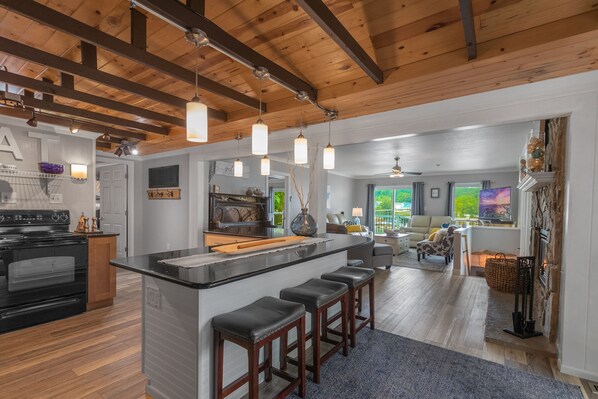 A modern kitchen with a central island, bar stools, and a dining area with a view.