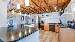 Una cocina moderna con una isla central, electrodomésticos de acero inoxidable, vigas de madera en el techo y una variedad de utensilios de cocina en estantes.