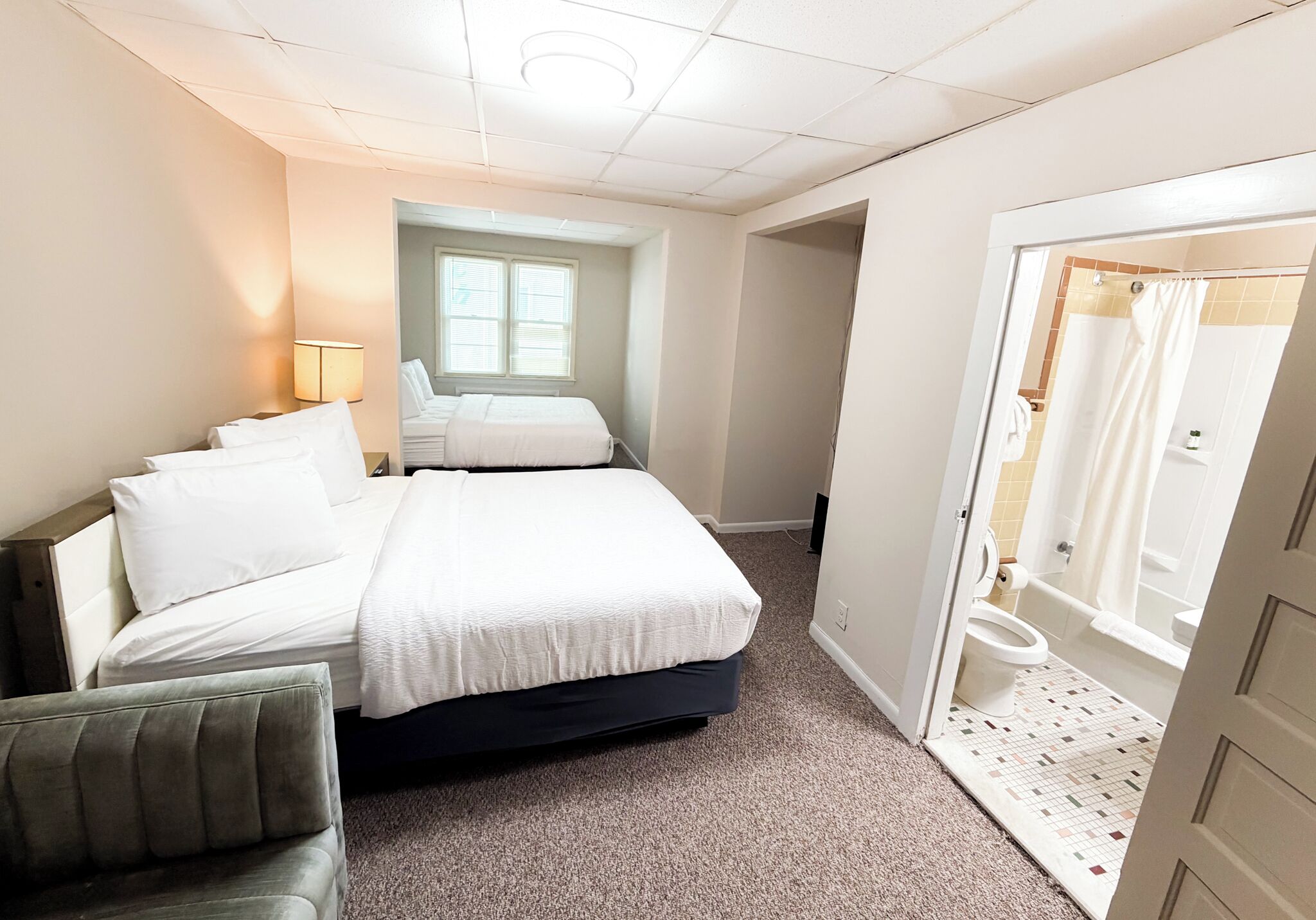 A hotel room with a bed, a chair, a window, and a bathroom visible through an open door.