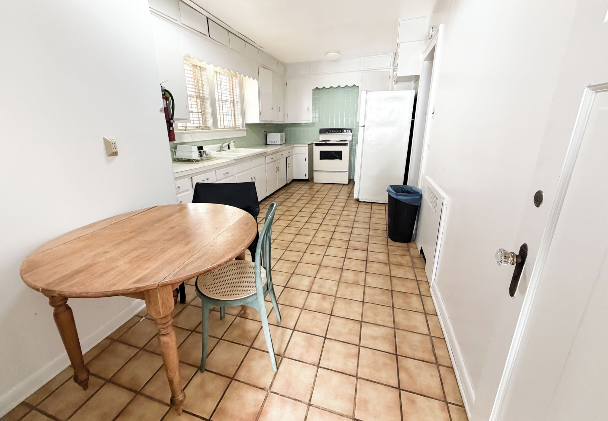 Une cuisine avec des meubles blancs, une table en bois, une chaise, une cuisinière et un réfrigérateur.