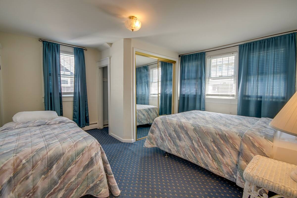 Habitación de hotel con dos camas, un espejo grande y una ventana con cortinas.