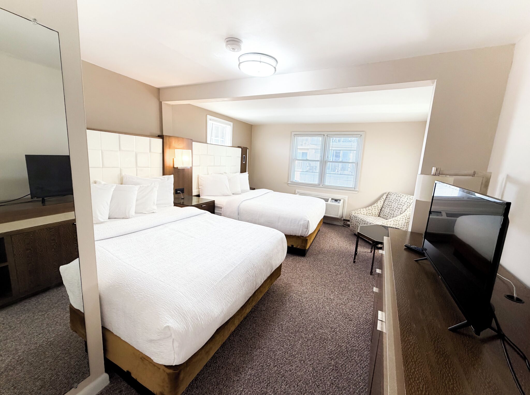 Ein Hotelzimmer mit zwei Betten, einem Fernseher, einem Schreibtisch und einem Sessel.