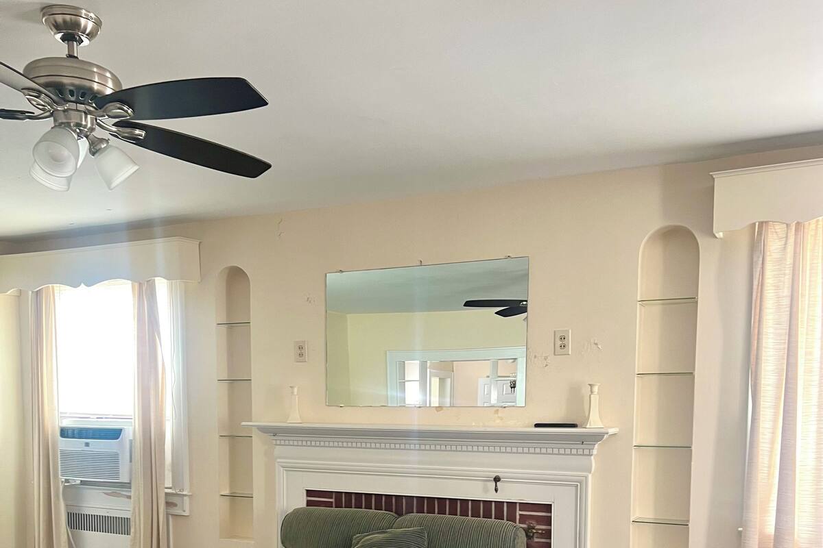 Una habitación con un sofá verde, chimenea, ventilador de techo y un espejo grande.
