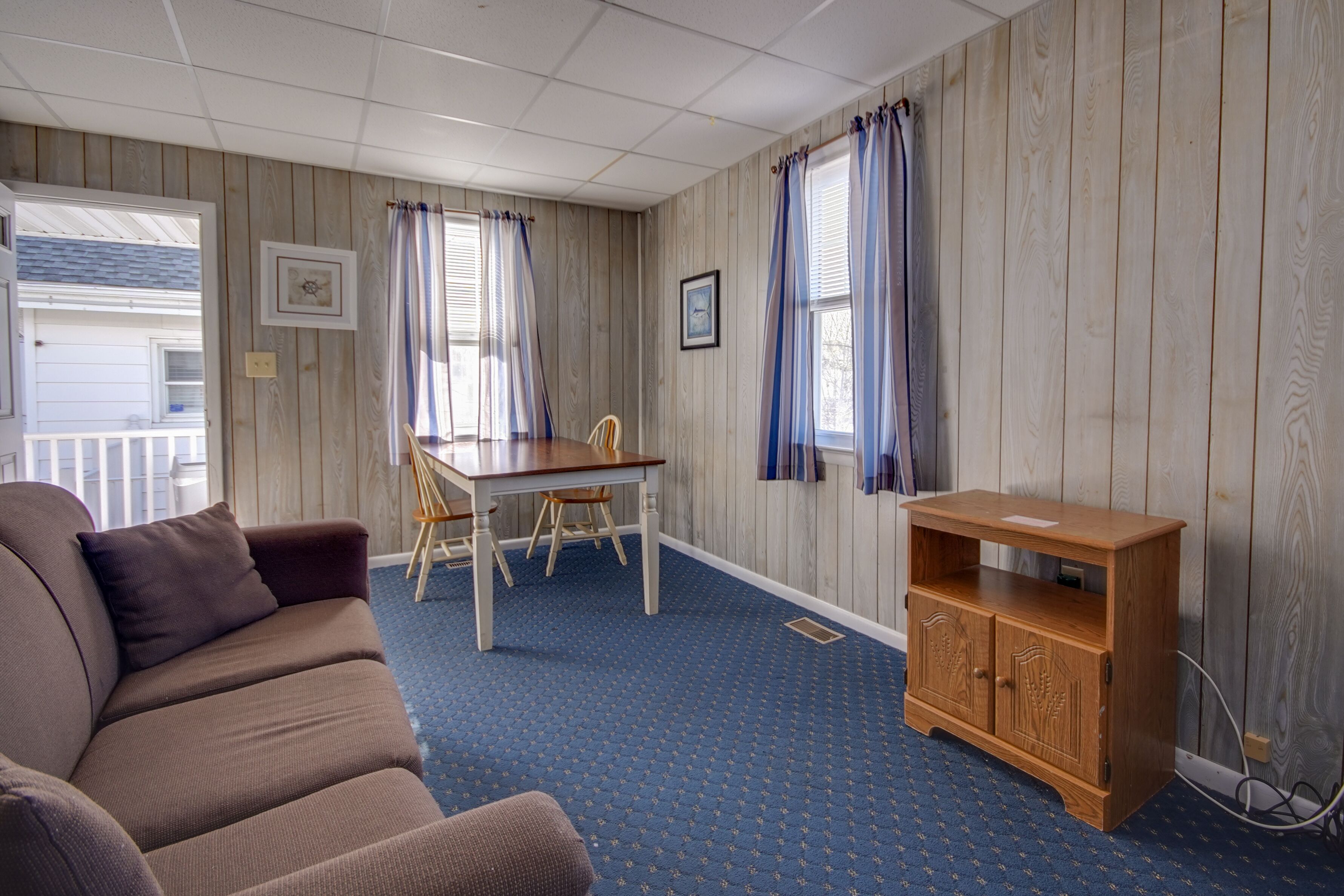 A room with a brown sofa, a dining table with chairs, a wooden cabinet, and a blue carpet.