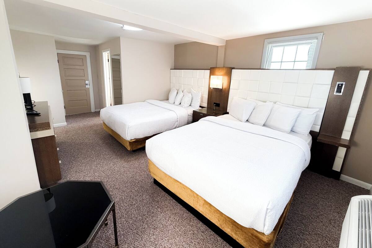 Una habitación de hotel con dos camas, un escritorio, una silla, una lámpara y una ventana.