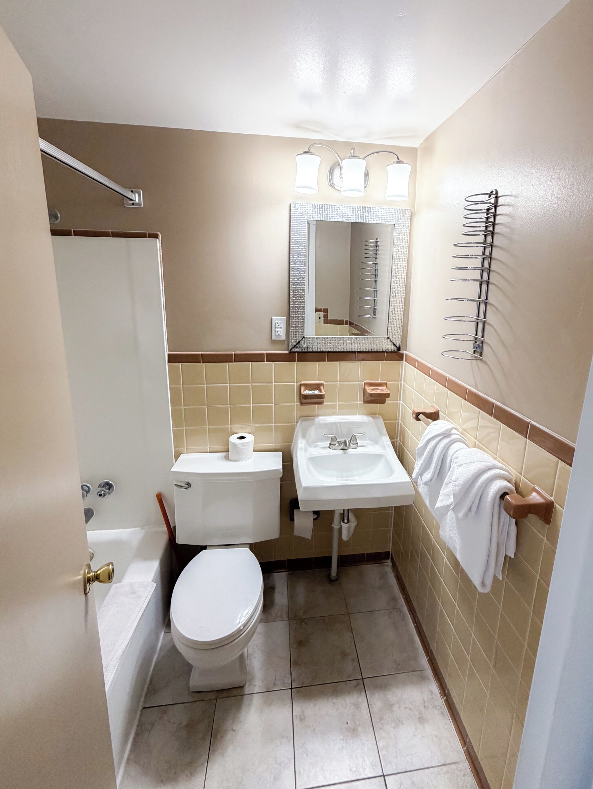 A bathroom with a toilet, sink, mirror, towel rack, and a shower area.