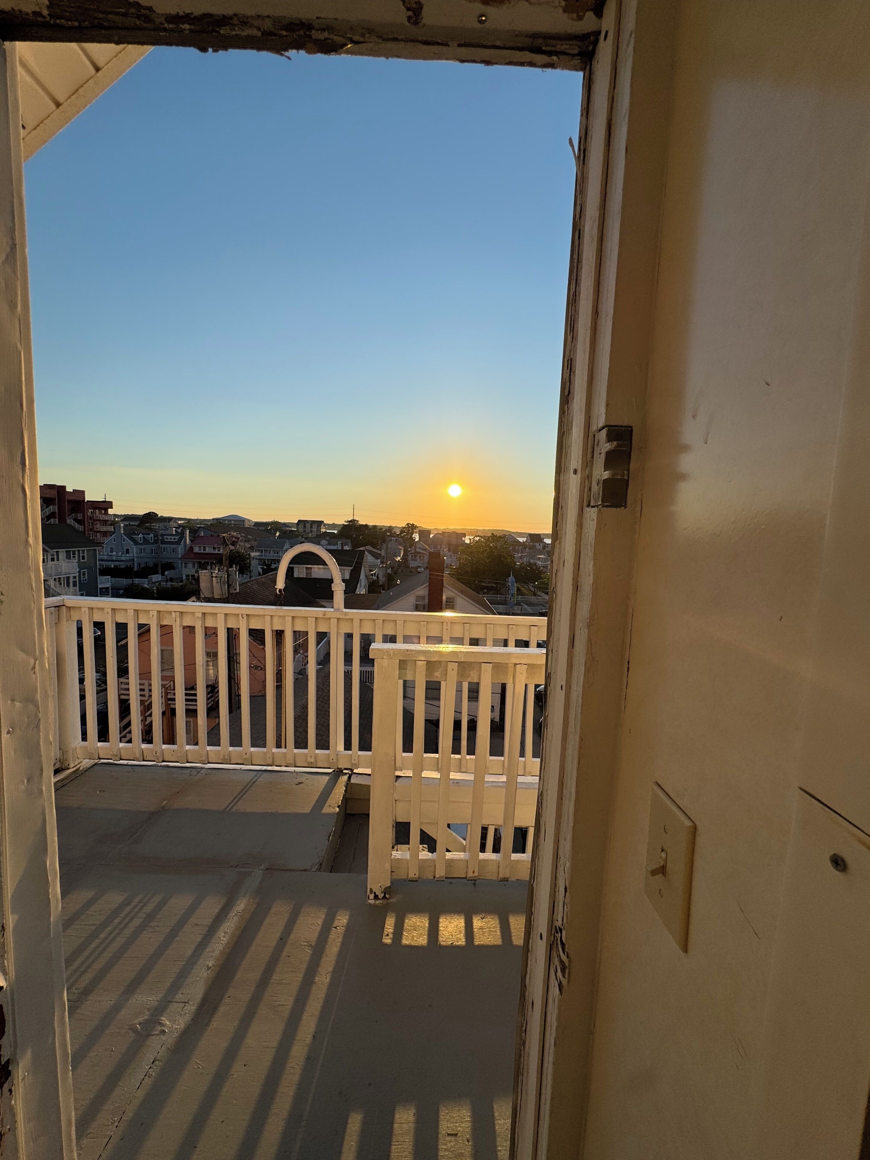 A balcony with a view of the sunset over a residential area.