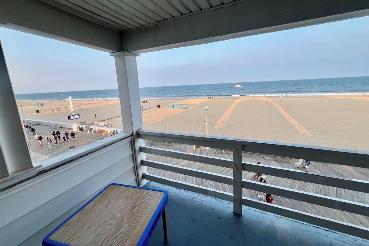 Vista a la playa desde un balcón cubierto con terraza de madera, un banco y barandilla.