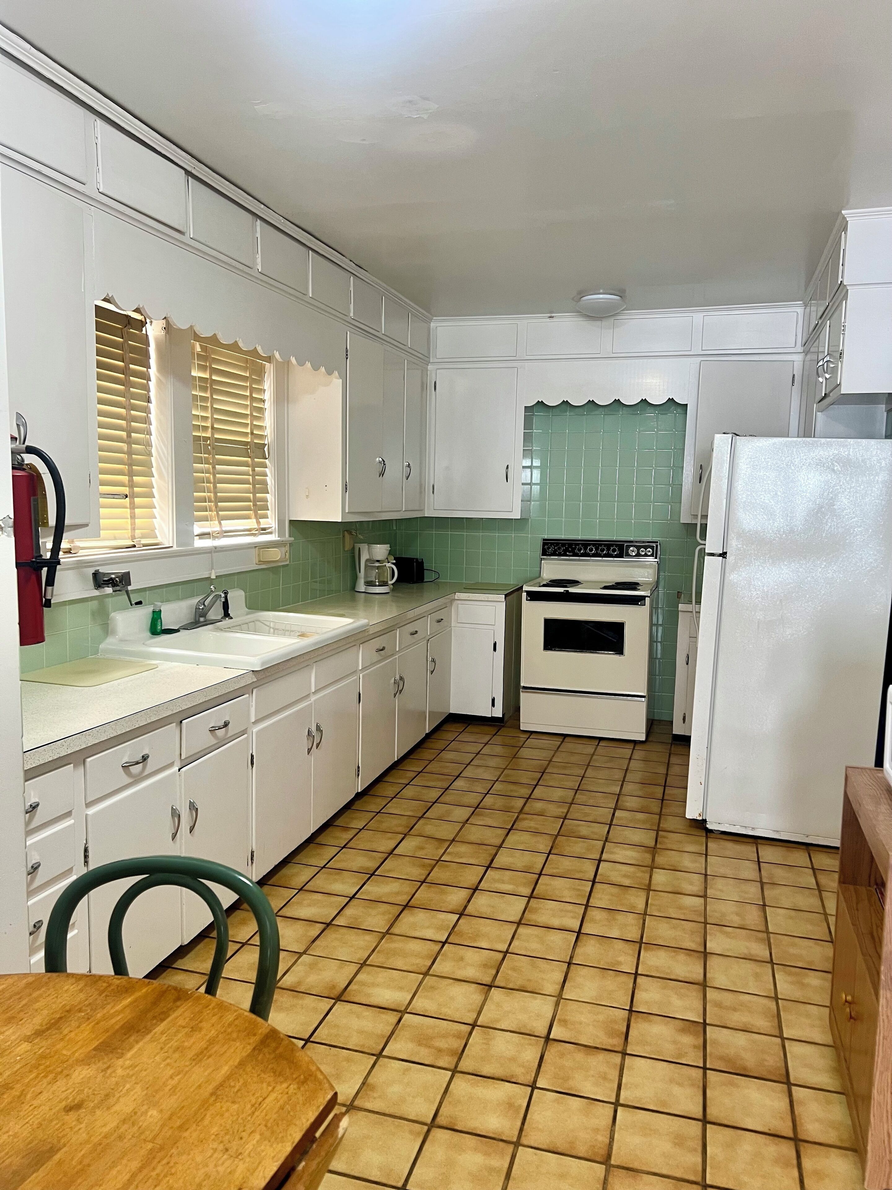 A kitchen with white cabinets, a stove, a sink, and a refrigerator.