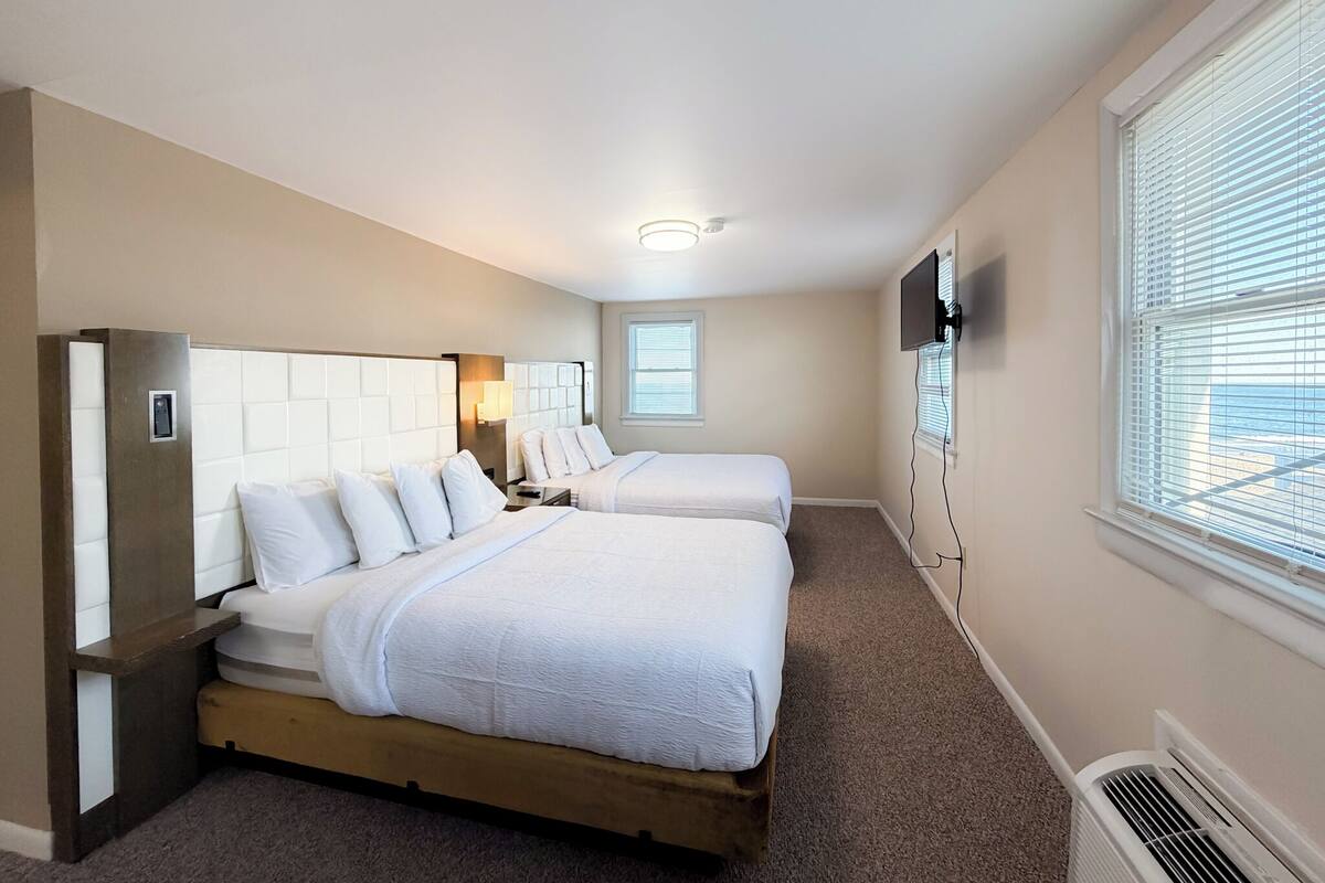 Una habitación de hotel con dos camas, un televisor montado en la pared y una ventana con persianas.