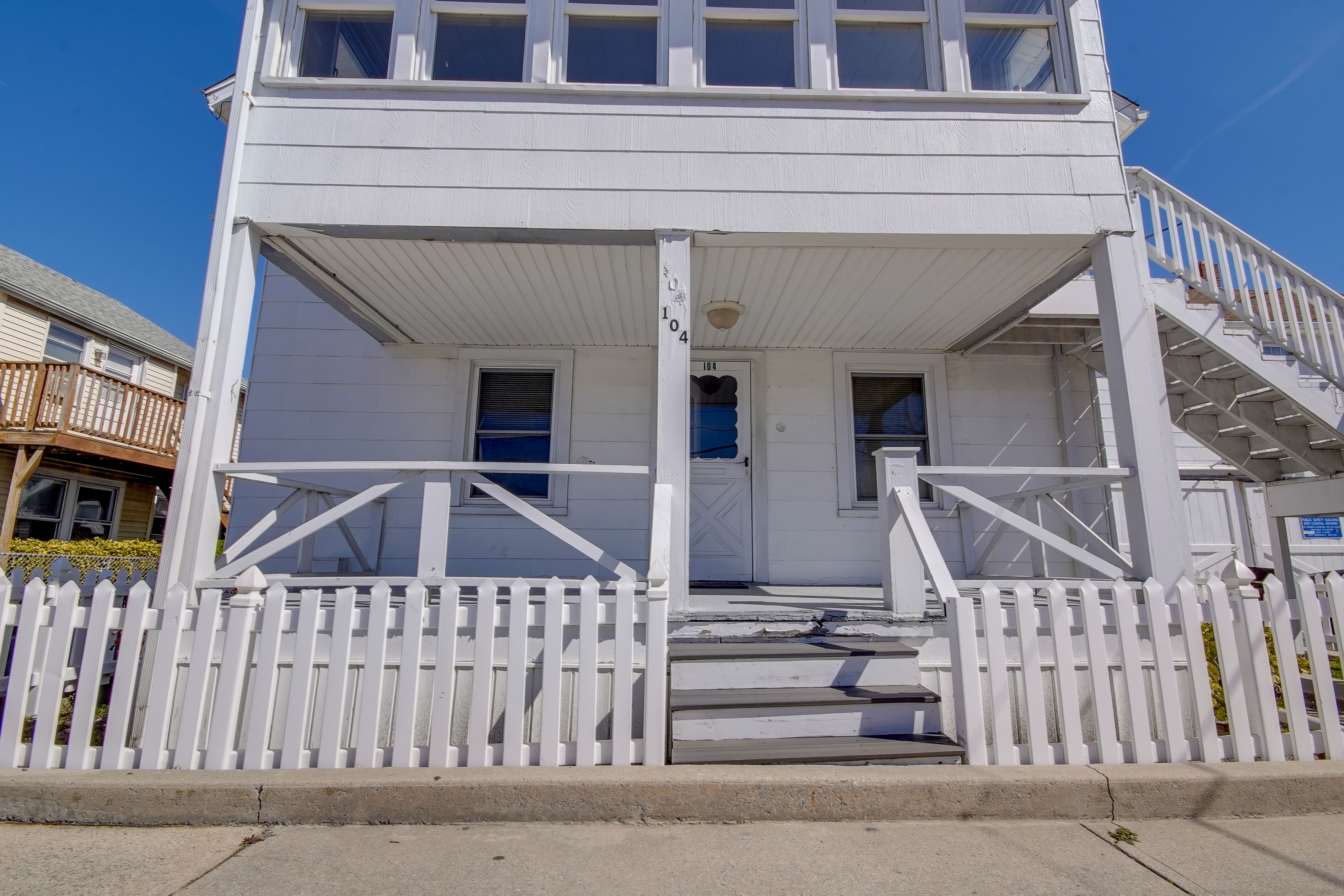 A white two-story building with a porch, a white picket fence, and a staircase leading to the upper floor.