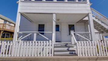 A white two-story building with a porch, a white picket fence, and a staircase leading to the upper floor.